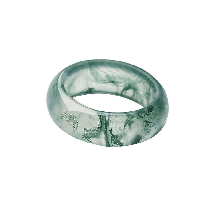 Handcrafted natural moss agate ring with distinct green inclusions displayed on a rich, dark wooden surface, highlighting the ring's organic beauty and intricate details.