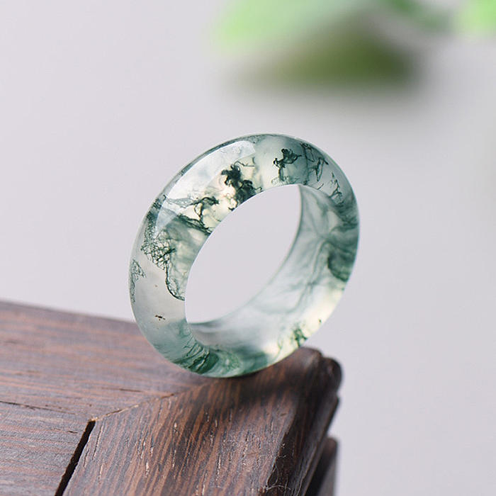 Handcrafted natural moss agate ring with distinct green inclusions displayed on a rich, dark wooden surface, highlighting the ring's organic beauty and intricate details.
