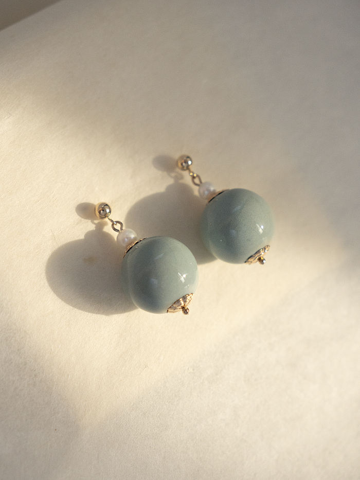 Flatlay of Celadon Tianqing Collection earrings with 14K gold floral caps and freshwater pearls, minimal aesthetic.

