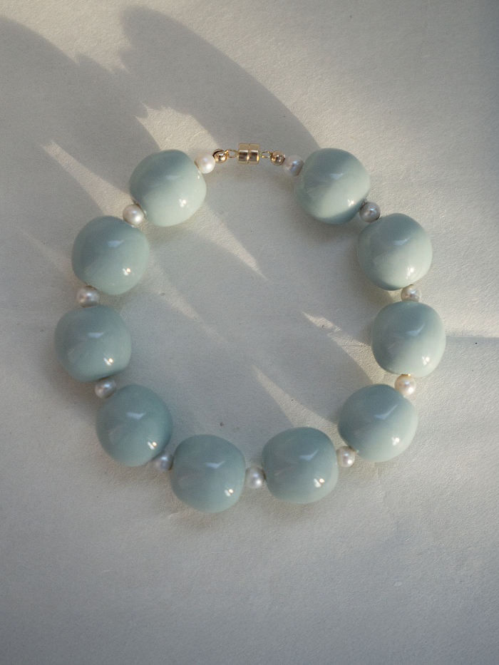 Top-down image of the bracelet in full closed form, resting on a pale surface, showing the symmetry and luminous finish of each bead.