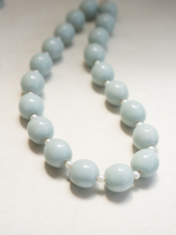Loosely coiled porcelain necklace under soft light, showing the fluidity and texture of celadon glaze.