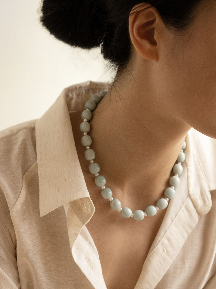 Frontal view of the Celadon Dew Necklace worn with a natural white shirt, showing balance of pearls and porcelain.