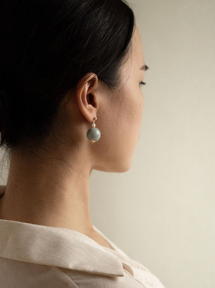 Natural daylight portrait featuring the earrings’ soft silhouette and gold pearl structure, worn with white linen collar.
