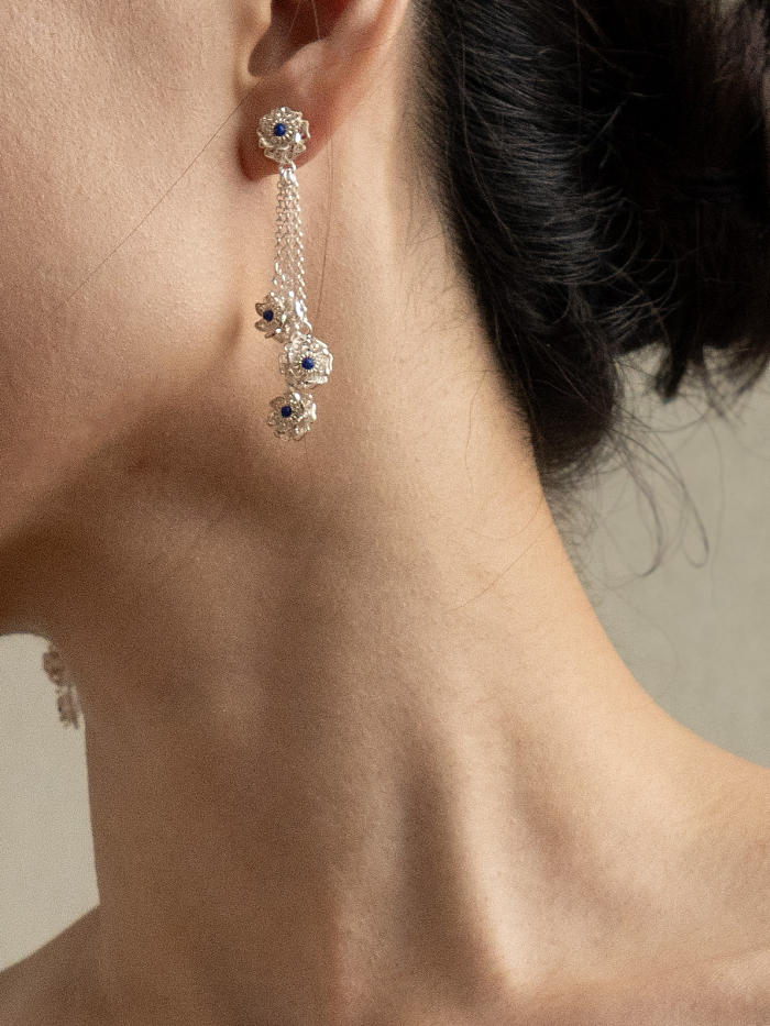 Side profile close-up showing the flowing movement of three silver chains with flower drops