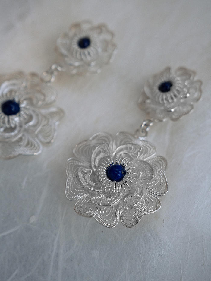 Angled view of silver filigree earrings with dimensional floral composition on translucent paper