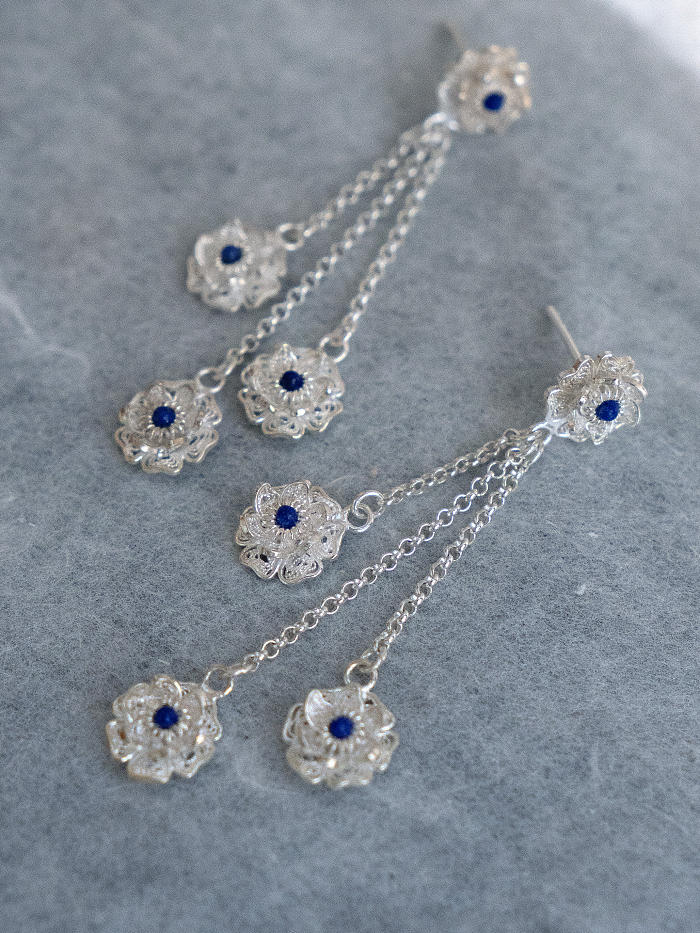 Flatlay of earrings on textured xuan paper, highlighting silver wirework and blue stones