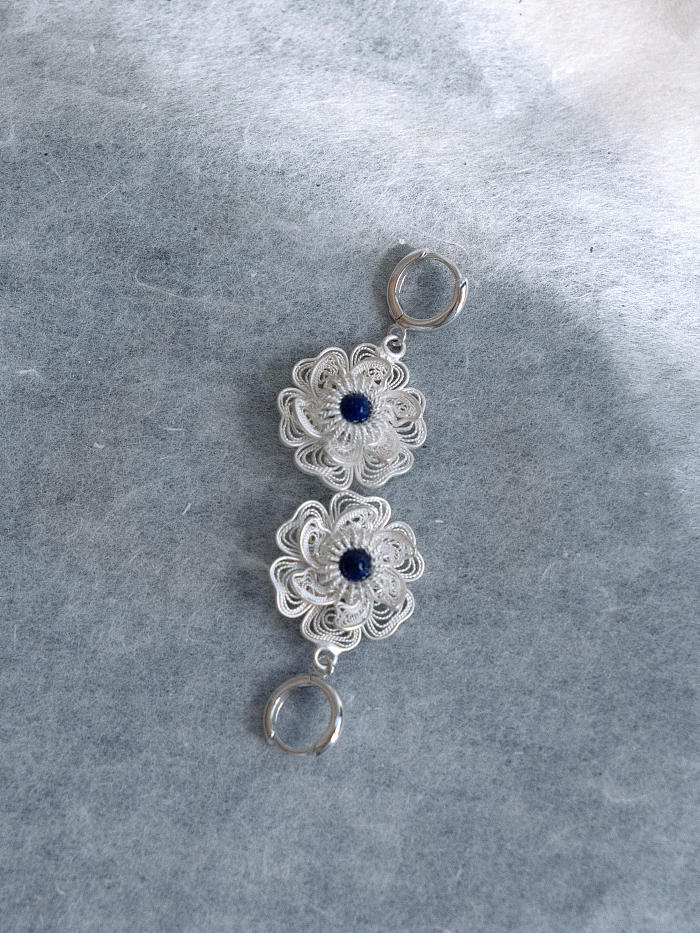 Top-down view of earrings on pale blue paper, highlighting filigree texture and lapis depth