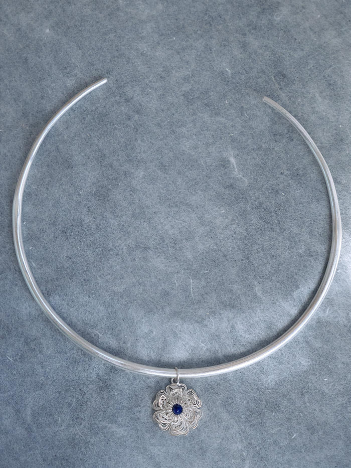 	Flatlay of silver collar with pendant on soft grey background, showing construction and contrast